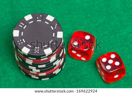 black and red poker chips and dice on a green casino felt