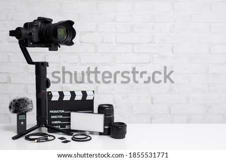 videography concept - modern dslr camera on 3-axis gimbal stabilizer, lenses, microphone, led light, clapper board and other videography equipment over white brick wall background with copy space Stock foto © 