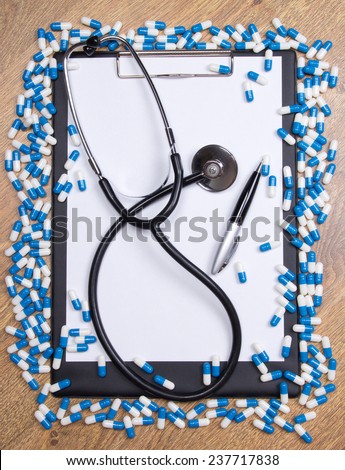 heal of blue tablets, clipboard, stethoscope and pen on wooden table
