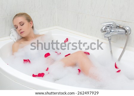 young beautiful sexy woman relaxing in bath with red flower petals