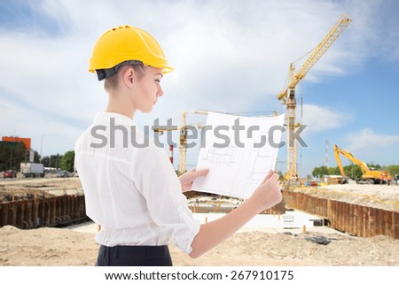 young business woman architect in yellow builder helmet with building plan at construction site