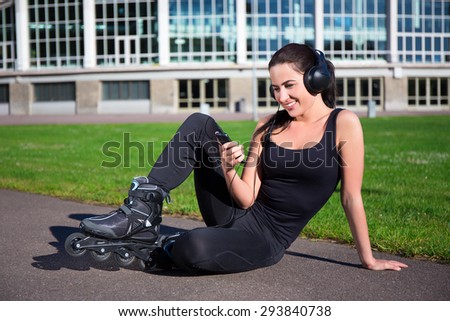 happy woman in roller skates sitting and listening music in summer park