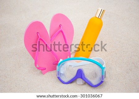 summer concept - diving mask, pink slippers and suntan lotion bottle on sandy beach