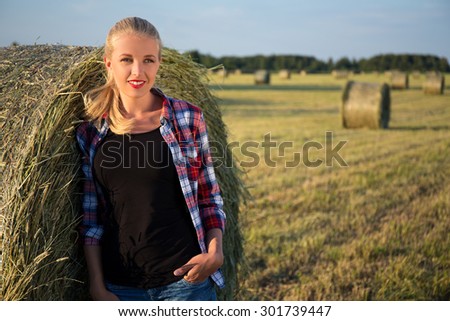 portrait of young beautiful blonde woman posing in field with haystacks