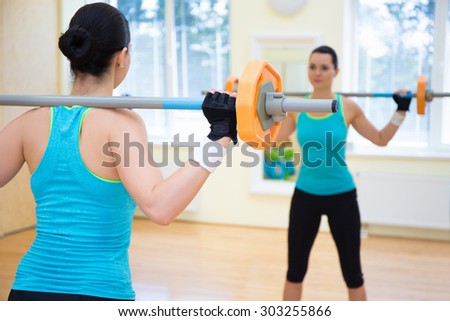 bodybuilding concept - back view of sporty woman exercising with barbell in gym