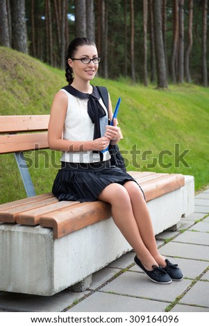 attractive school girl or student sitting on bench in summer park