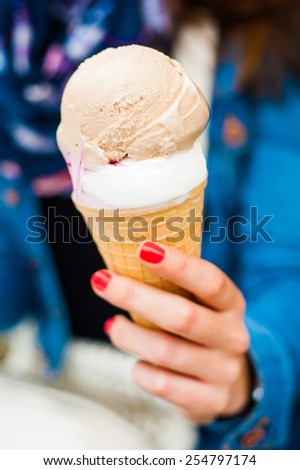 Cold titbit sweet hazelnut and vanilla ice cream scoops in crispy cone in red nailed young womans hand