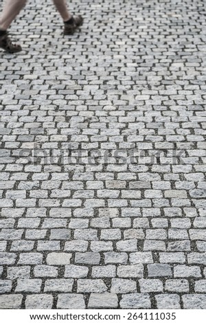 Detail of a man walking on cobblestone pavement on the street