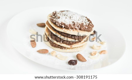 American styled oat pancake filled with zucchini based sugar free raw chocolate and grated coconut decorated with nuts on white plate and background