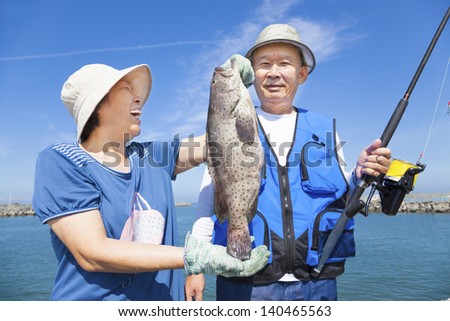 happy asian senior couple fishing and showing big grouper