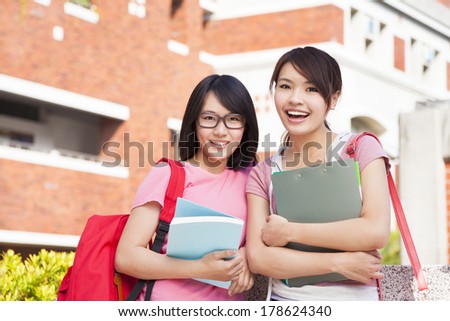 two smiling students holding books  on campus