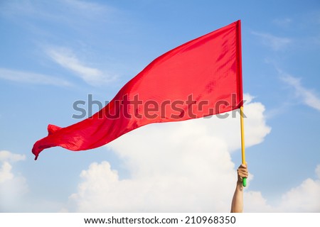 Hand waving a red flag with blue sky background