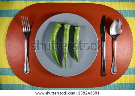 An Okra or Lady\'s Finger on a Plate A photo of an okra or lady finger on a plate setting with utensils