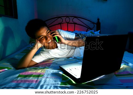 Young Teen in front of a laptop computer and on a bed and using a cellphone or smartphone Photo of a Young Teen in front of a laptop computer and on a bed and using a cellphone or smartphone