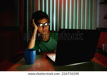 Young Teen with eyeglasses and bored in front of a laptop computer Photo of a Young Teen with eyeglasses and bored in front of a laptop computer