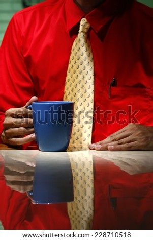 Man wearing red long sleeve shirt, yellow necktie and holding a coffee mug Photo of a man wearing red long sleeve polo shirt and holding his yellow necktie and holding a coffee mug.