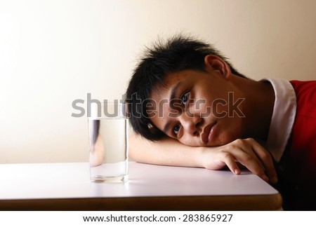 Teen looking at a glass of water on a wooden table Photo of a Teen looking at a glass of water on a wooden table