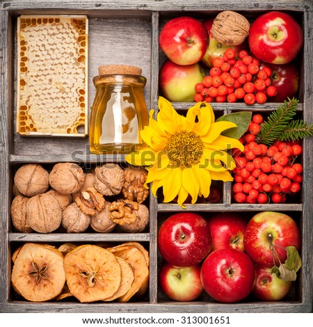 Autumn harvest. Composition in wooden box. Honey, Red apples, nuts, flowers, sunflowers, dried apples