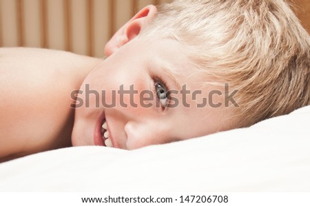Portrait of little boy lying in the bed. Just awakened happy boy.