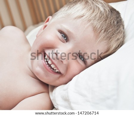 Portrait of little boy lying in the bed. Just awakened happy boy.