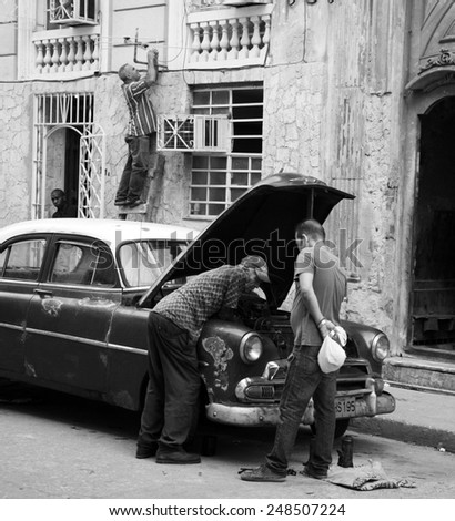 HAVANA, CUBA - APRIL 5, 2014: Cuban men leaning over the hood of an old car and a man up a ladder connecting an aerial.