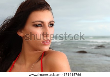 A beautiful brunette on the beach is gazing into the distance.