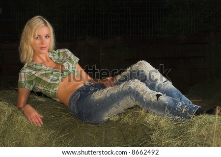 a blond lady is lying down on lucern hay bale, she is the real dream farmer girl