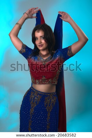 a beautiful East Indian lady dressed in a traditional sari outfit is standing holding a scarf behind her