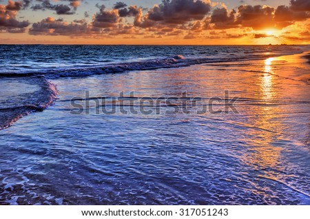 Sun casts an orange hue on the horizon, above the clear water