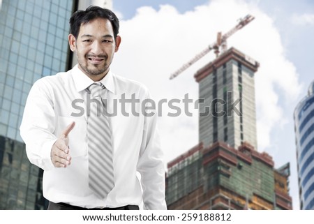 handsome businessman with open hand ready for handshake with the blur construction site background