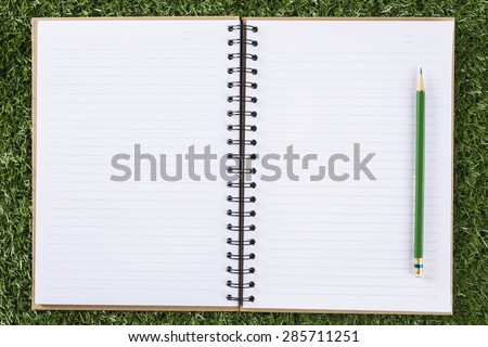 notebook paper background with pencil on green grass background