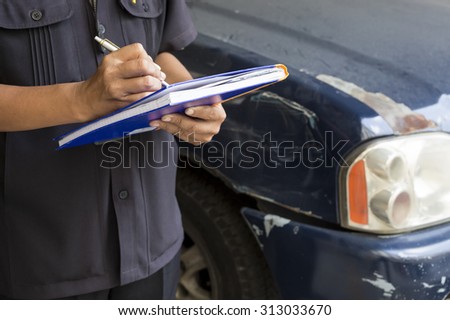 Side view of writing on paper while insurance agent examining car after accident