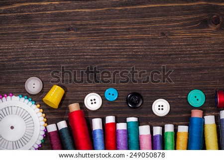 Scissors, bobbins with thread and needles on the old wooden background. Vintage Background