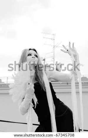 black-and-white photo of a Pretty red-haired girl with feathers, bandages and fan on rooftop