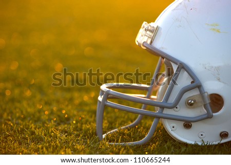 American Football Helmet on the Field with room for copy backlit by the setting sun