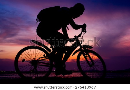 Silhouette of backpacker ride mountain bike on bridge beside sea with sunset sky background