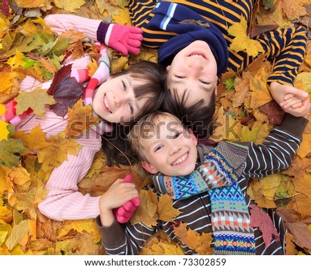 Three siblings laying in autumn leaves.