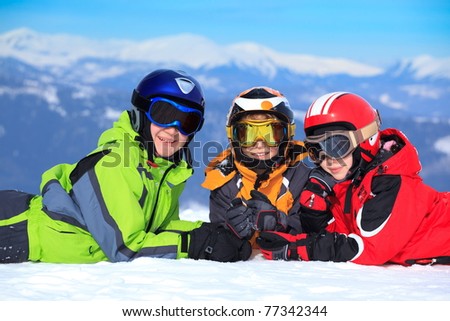 Two happy brothers with sister in ski helmets and goggles on snowy Alpine mountain.