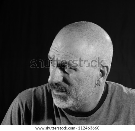 Black and white profile of an older bald man with facial hair looking off to the side looking concerned.