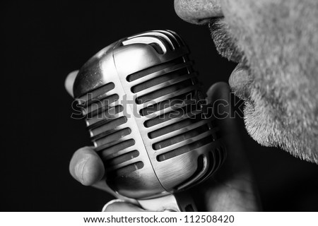 Close up of a singers mouth singing into a vintage microphone with a black background