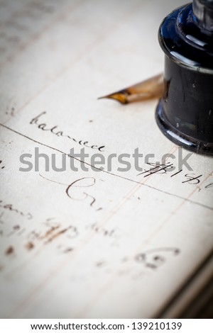 Close up of a page out of an antique accounting ledger with an old feather quill pen and an antique glass inkwell