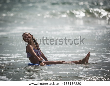 Young girl sitting on a boogie board in the ocean with her head tilted back smiling at Sunset Beach in Southern California