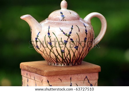 A glazed clay teapot with blue flower motif before green background.