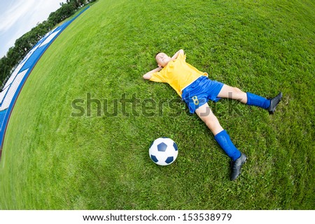 Dreaming boy soccer player lying on natural grass. Fish-eye lens.