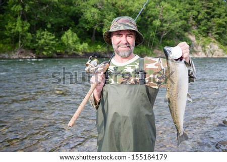 Joyful fisherman holds caught pink salmon in the river.