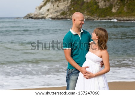 Happy pregnant woman and her husband strolling by the sea.