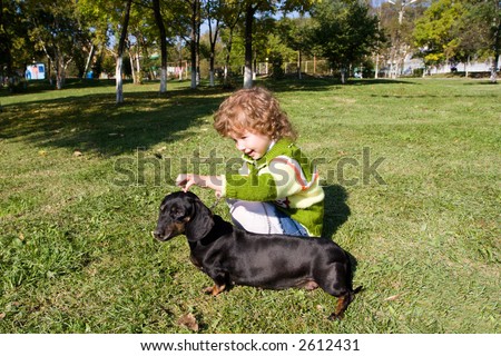 The little girl walks with a dog (dachshund) in park.