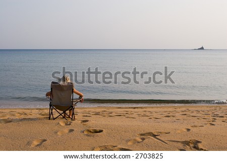 Lady sits on a chair at the sea in the autumn evening.Above horizon white overcast.