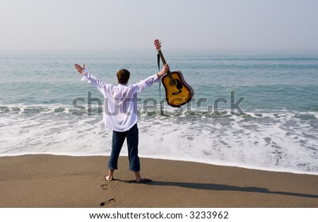 The young guy (musician) walks on a beach with a guitar.