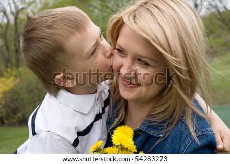 Son kisses mother. In his hand the boy flower dandelion.